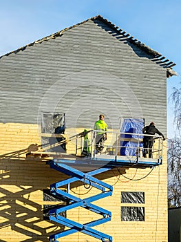 Residential house facade painting works after cladding with wooden planks using scissor lift platform