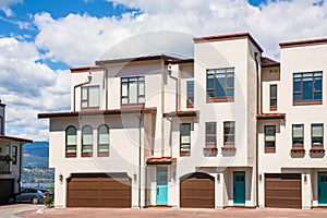 Residential townhouses with scenery view on a lake and mountains. Townhomes with wide garage door and cars parked in front.