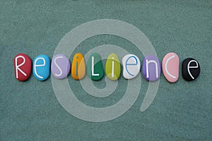 Resilience word composed with multicolored handmade painted stone letters over green sand