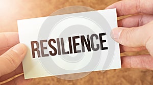 resilience word inscription on white card paper sheet in hands of a businessman. recap concept. red and white paper