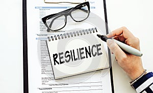 Resilience word written on notepad on a table with woman hand and marker