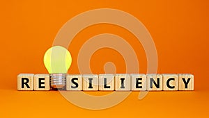 Resiliency symbol. Wooden cubes with word `resiliency`. Yellow light bulb. Beautiful orange background. Business and resiliency