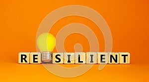 Resilient symbol. Wooden cubes with word `resilient`. Yellow light bulb. Beautiful orange background. Business and resilient photo