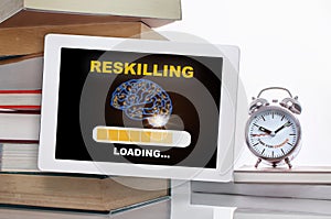 Reskilling loading with brain on digital computer tablet with stack of textbook with time to change words on alarm clock