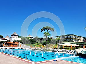 Scene with swimming pools, lounge chaires, pine and palm trees and hotel building photo