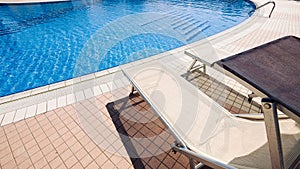 Resort pool. Summer resort chair, relax lounge at luxury hotel pool. Beach lounger chaise. Vacation sunbed. Blue water
