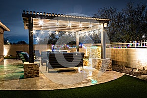 A resort style backyard at night with a waterfall, pergola, and a firepit photo