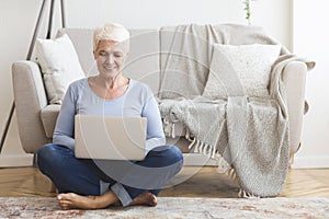 Resourceful mature woman sitting on floor and using laptop