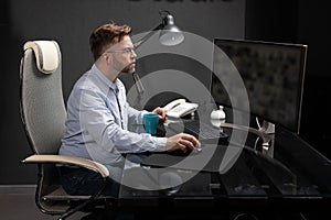 Business man with glasses working in office at computer table and drinking coffee from bright Cup