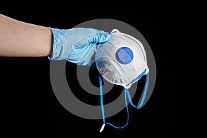 Respirator FFP2 in hand in blue rubber glove, isolated on black background