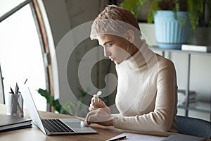 Responsible young woman wiping computer keyboard touchpad with antibacterial liquid.