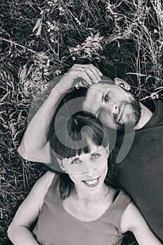 Couple makes a selfie while lying on the grass in flowers. Rest, lovers on a flower meadow. Bearded man and a girl in a red dress