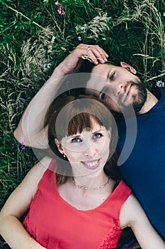 Couple makes a selfie while lying on the grass in flowers. Rest, lovers on a flower meadow. Bearded man and a girl in a red dress