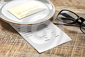 Restaurant bill paying by card and glasses on wooden table background