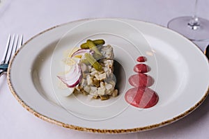 Restaurant delicacy dish on a purple tablecloth. White plate with herring