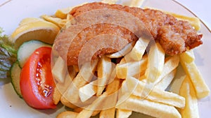 Restaurant food. Chop in batter with french fries cut slice of tomato, lemon and cucumber on a large plate close up view