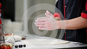 Restaurant kitchen. A chef clapping his hands with flour on it. Preparing a dough for the pizza