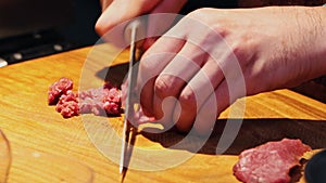 Restaurant kitchen - chef cutting meat in small pieces with sharpened knife