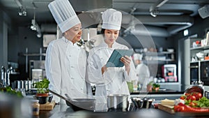 Restaurant Kitchen: Team of Asian and Black Female Chefs use Tablet Computer while Cooking Delicious