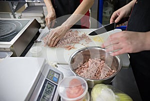 Restaurant kitchen. Two men workers cutting sausages and putting it in the pot