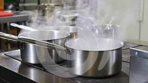 Restaurant kitchen video. Boiling saucepans on massive stove. Busy staff rushing. White steam from hot water. Chef