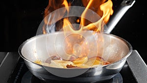 Restaurant open kitchen show. Slow motion food video. Chef cooking with flame in a frying pan on kitchen stove. Flambe
