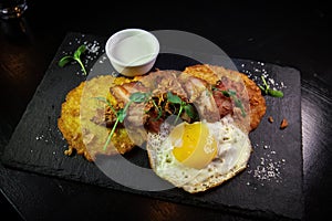 Restaurant serving snacks on the board - potato pancakes with fried meat and egg. A bowl with sauce and a glass of vodka