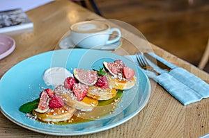 Restaurant sweet breakfast. Small pancakes with caramel cream and strawberries, figs, raspberries, fruit on top. a cup of a coffee