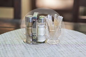 In the restaurant on the table in a glass, the toothpicks are laid on a white place setting and next to them is a salt shaker