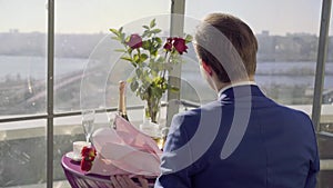 Restaurant table on the roof with amazing river wiev, man in suit sit on this table with roses and waiting for his woman