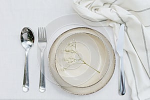 Tableware and silverware setting on white tablecloth, top view