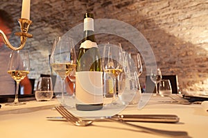 Restaurant table with vintage silverware, bottle of white wine with blank label, glasses, cutlery, gold candlestick, degustation