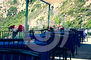 Restaurant tables with black chairs red and white flowers and blue tablecloth in a natural environment. Peaceful place to have foo