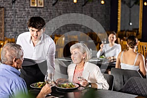 Restaurateur guy serves customers elderly spouses plate with dinner order