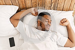 Rested African Guy Waking Stretching Hands Awakening In Cozy Bedroom