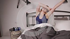 Rested positive attractive mature woman waking up and stretching arms in bed