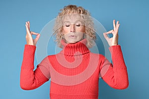 Restful blonde female in red sweater feels relaxed, tries to concentrate