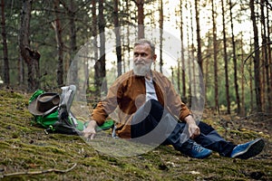 Restful mature man hiker enjoying halt in forest during trip adventure