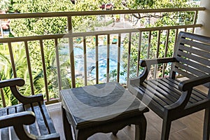 resting area of balcony with two couch armchair sofa outdoor. high view. sun deck of resort. Swimming pool view and palm trees.