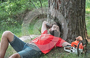 Resting after hard work. Lumberjack worker with chainsaw in the forest. Man doing mans job. Logging. Harvest of timber