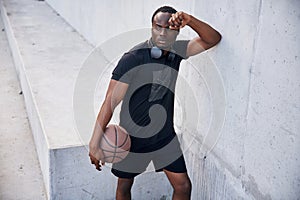 Resting by leaning on the white wall. Young black man is with basketball ball outdoors