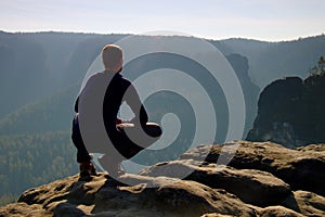 Resting man at the top of rock with aerial view of the deep misty valley bellow