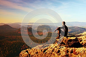 Resting man at the top of rock with aerial view of the deep misty valley bellow