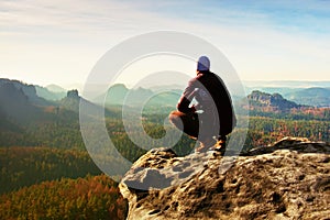 Resting man at the top of rock with aerial view of the deep misty valley bellow