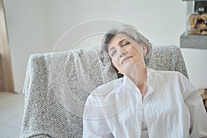 Resting smiling elderly woman reclining on a comfy sofa stretching, calm, meditating