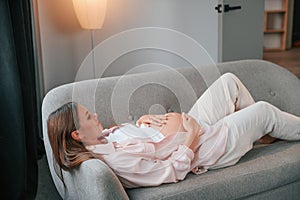 Resting on the sofa. Beautiful pregnant woman is indoors at home