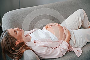 Resting on the sofa. Beautiful pregnant woman is indoors at home