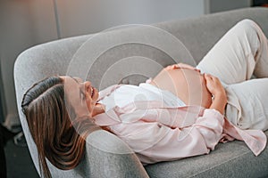 Resting on the sofa. Beautiful pregnant woman is indoors at home