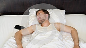 Restless man waking up with headache, lying in bed early in morning, top view