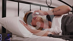 Restless mature woman in sleep mask waking up in bed, disturbed by noise